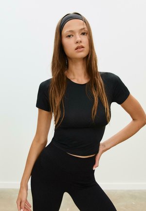 Haut noir ajusté à manches courtes associé à des leggings noir taille haute. Tissu lisse et extensible, présentant un éclat subtil et des coutures minimales.