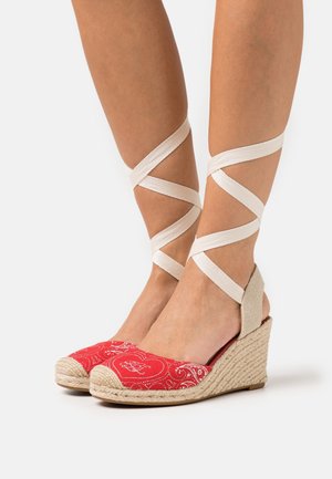 Sandales compensées espadrilles rouges avec une tige en tissu à motif, semelle en corde naturelle et brides croisées beiges à la cheville. Bout plat et design arrondi.