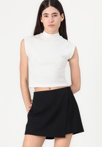 Hvit, ermeløs, høyhalset crop top kombinert med et svart, A-linjeet mini skjørt med en sidelpleat detalj. Glatt stoff, minimalistisk design.