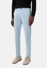 Lichtblauwe broek met een rechte pijp, gemaakt van een gladde stof. Heeft zijzakken en een knoopsluiting. Gecombineerd met beige sneakers.