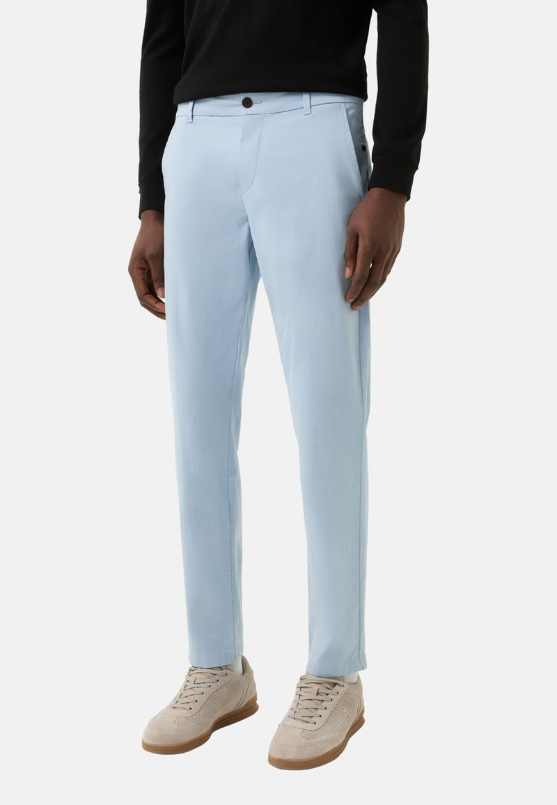 Lichtblauwe broek met een rechte pijp, gemaakt van een gladde stof. Heeft zijzakken en een knoopsluiting. Gecombineerd met beige sneakers.