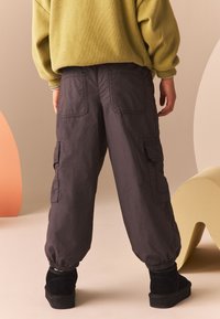 Pantaloni cargo grigio scuro con polsini elastici, molteplici tasche e una vestibilità rilassata. Indossati con calzature nere e un maglione oversize verde oliva.