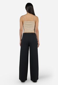 Beige ribbed crop top with thin straps paired with high-waisted wide-leg black trousers, made from a smooth fabric.
