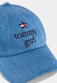 Blå denimkeps med broderad "tommy girl" text och en stjärnlogotyp med svarta, vita och röda detaljer. Böjd skärm och texturerad yta.