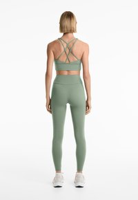 Ljusgrön sport-bh med korsade remmar och matchande högmidjade leggings, tillverkade av ett mjukt och elastiskt tyg.