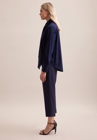Navyblauw op maat gemaakt shirt en bijpassende cropped broek van gladde stof, met een puntige kraag en knoopmanchetten, gecombineerd met zwarte hakken.