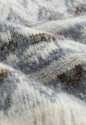 Szürke, fehér és barna fonalak keverékéből kötött pulóver. Textúrált mintázattal rendelkezik, amely a szálak vastagságának és puhaságának változataival díszített.