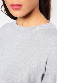 Hellgrauer, gestrickter Pullover mit Rundhalsausschnitt und gerippten Bündchen. Der Stoff hat eine weiche Textur und verfügt über einen leichten Stretch.