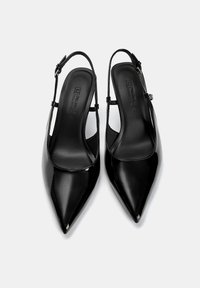 Chaussures slingback en cuir verni noir avec un bout pointu, une fine sangle à la cheville et une texture lisse. L'intérieur présente un logo en relief.