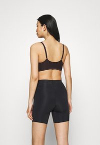 Brown sports bra with adjustable straps and seamless design, paired with black high-waisted shorts featuring dotted detailing near the waistband.