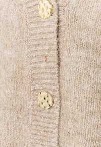 Beige strikket cardigan med en myk tekstur, med et ribbet design og to gullfargede, hamrede metallknapper.
