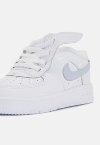 Bele krožne športne superge z belim usnjem in svetlo sivo Nike ikono. Imajo podložen jezik in zavezovanje z vezalkami. Gumijast podplat z teksturo in prezračevalnimi otvori.