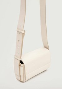 Pequeño bolso cruzado de cuero color crema con forma rectangular y correa ajustable con agujeros para hebilla de metal.