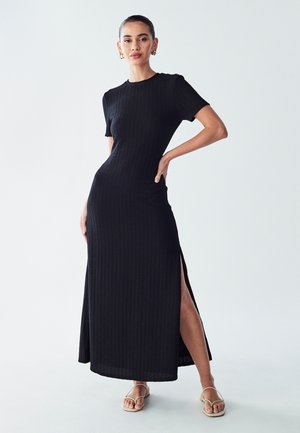 Musta neule pitkä mekko lyhyillä hihoilla, jossa on tekstituottumusteksti ja korkeat sivuraot. Yhdistetty minimalistisiin sandaaleihin.