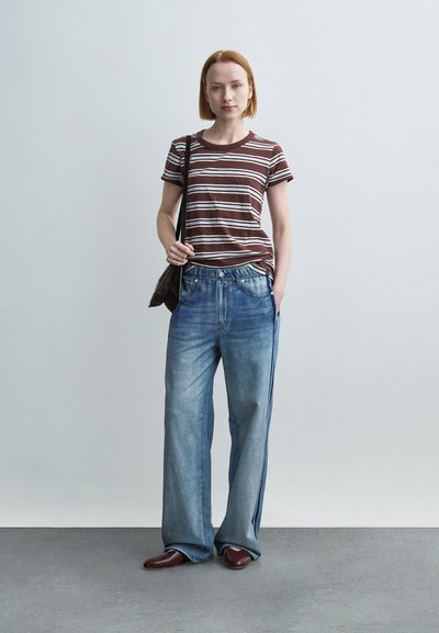 Ριγέ καφέ και λευκό t-shirt, άνετο τζιν παντελόνι σε μπλε απόχρωση με ίσια γραμμή και μπορντό παπούτσια. Μαύρη τσάντα ώμου συμπληρώνει την εμφάνιση.