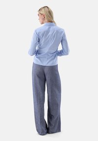 Light blue button-up shirt with a structured collar, paired with loose-fitting dark blue textured trousers. Back view shows subtle seam details.