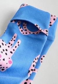 Blå sokker med lyserøde, tegneserieagtige designs med sorte pletter og detaljer. Lavet af blødt stof med en glat tekstur.