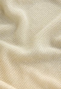 Strukturiertes beiges Gewebe mit einem gewebten Muster, das weiche, feine Fäden aufweist, die einen dezenten Schimmer und einen dreidimensionalen Effekt erzeugen.