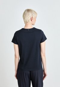 Svart kortermet t-skjorte laget av myk, elastisk stoff med rund hals. Har en liten metallisk detalj på baksiden.