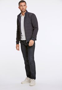 Marinblå zip-jacka med texturerad kropp, enfärgade ärmar, vit kragskjorta, mörka jeans och ljusa sneakers, med en åtsittande design.