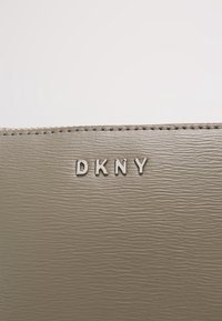 Portafoglio in pelle beige testurizzata con logo "DKNY" metallico in rilievo. Presenta una finitura liscia e cuciture sottili lungo il bordo.