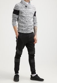 Texturerad grå och svart stickad tröja med krage, svarta paneldetaljer på ärmarna. Svarta joggbyxor med ribbade knädetaljer och svarta skor.