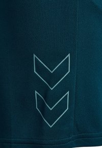 Camisa deportiva en un tono azul oscuro con un tejido texturizado y un diseño de logo en forma de chevron en azul claro cerca del dobladillo.
