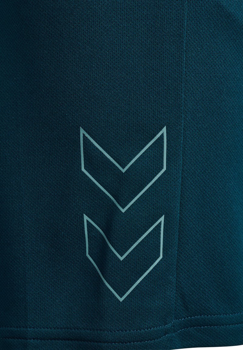 Camisa deportiva en un tono azul oscuro con un tejido texturizado y un diseño de logo en forma de chevron en azul claro cerca del dobladillo.