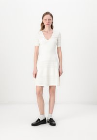 White short-sleeve dress with a V-neck, textured knit design, fitted bodice, and flared skirt. Paired with black loafers and gray socks.
