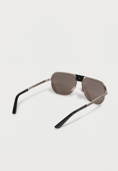 Γυαλιά ηλίου με καφέ σκουρόχρωμους ορθογώνιους φακούς, ασημένιο μεταλλικό πλαίσιο, μαύρες άκρες στους βραχίονες και διακοσμητικά ασημένια μπράτσα, τοποθετημένα πάνω σε λευκή επιφάνεια.