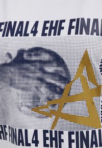 Biała koszulka z granatowym i złotym wzorem graficznym. Zawiera napis "FINAL 4 EHF FINAL". Obecne są okrągłe i liniowe wzory kropek.