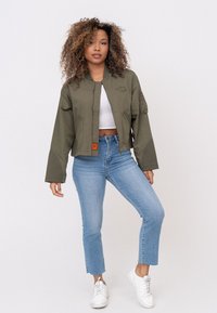 Olivgrüne, kurz geschnittene Bomberjacke mit glatter Oberfläche, ausgestattet mit einem Frontreißverschluss, Seitentaschen und bestickten Logodetails.