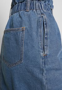 Blå denimshorts har en elastisk midja, sidofickor och en bakficka med synliga sömmar och en slät yta.