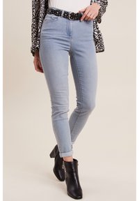 Jean skinny bleu clair à taille haute, doté d'une ceinture à pois noirs. Texture en denim lisse, longueur cheville avec ourlets roulés, porté avec des bottes noires.