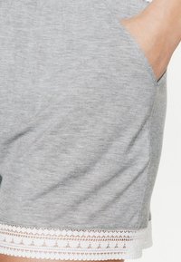 Shorts en coton gris avec poches latérales, ornés d'une bordure en dentelle blanche au bas, mettant en valeur la texture et un motif délicat.