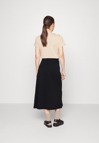 Top bege de mangas curtas combinado com uma saia longa preta, apresentando um design de cor sólida. Usado com sandálias pretas e meias castanhas.