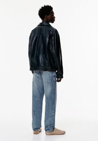 Črna usnjena jakna, ohlapne svetlo modre denim hlače in bež superge. Jakna ima ovratnik in pritrditev s pritisnim gumbom.
