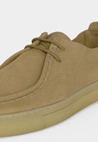 Καφέ σουέντ casual παπούτσι με στρογγυλεμένη μύτη, ελάχιστες ραφές και κορδόνια στο ίδιο χρώμα, με ανοιχτό μπεζ λαστιχένια σόλα.