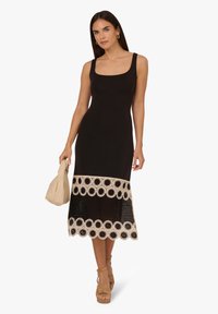 Abito nero con scollo quadrato, parte superiore aderente e orlo in pizzo uncinetto con motivi circolari in beige. Accentuato da una borsa leggera.