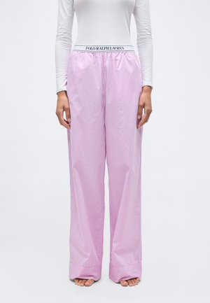 Femme portant un pantalon à jambes larges rayé rose et blanc avec une ceinture marquée "Polo Ralph Lauren" et un haut blanc cintré à manches longues.