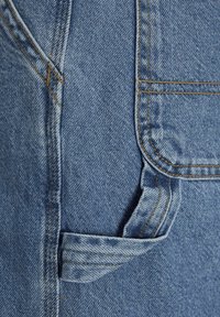 Tessuto denim di colore azzurro chiaro, con una tasca con flap piegato e cuciture gialle a contrasto lungo le cuciture.