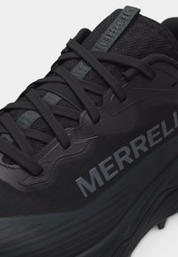 Κοντινή λήψη μαύρου αθλητικού παπουτσιού Merrell που δείχνει υφασμάτινη υφή, μαύρα κορδόνια και ανάγλυφο λογότυπο της μάρκας στο πλάι.