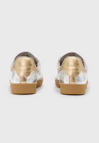 Sølv- og gullmetalliske sneakers med lavt design, teksturerte gummisåler i tan farge, og en glatt skinnfinish. Baksiden har preget tekst.