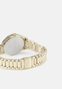 Montre en acier inoxydable doré avec un boîtier rond, un bracelet métallique et une fermeture à fermoir. Logo gravé au dos du boîtier.