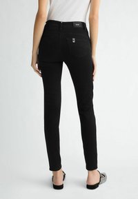 Jean skinny noir en denim, avec une taille mi-haute, poches arrière et une texture lisse. Porté avec des sandales à lanières.