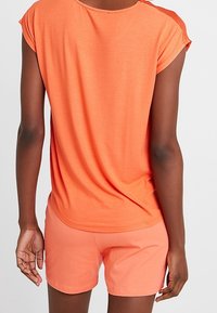 Top a maniche corte e collo rotondo e pantaloni corti in un vivace corallo, realizzati in tessuto leggero. L'outfit presenta una vestibilità comoda e una texture morbida.
