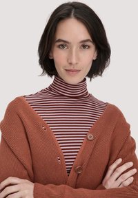Kastanienfarbener gestrickter Cardigan mit zwei Knöpfen über einem maroon-weißen gestreiften Rollkragenpullover. Glatte Textur, lockere Passform und geschichtetes Design.