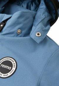 Giacca impermeabile blu per bambini con bottoni a pressione vicino al colletto e un patch rotondo in bianco e nero con il logo "reima weatherproof kids".