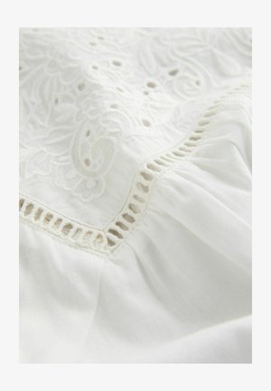 Weißer Stoff mit aufwändigen Stickmustern, die entlang des Randes ausgeschnittene Details aufweisen, sowie einer weichen, strukturierten Oberfläche. Leicht und zart.