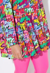 Buntes Kleid mit einem Muster aus variierter Handschrift in rosa, grün und blauen Tönen; hat ein ausgestelltes Design. Rosa Leggings darunter.